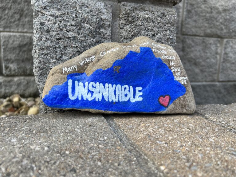 rock with blue paint shaped like Kentucky with the word Unsinkable